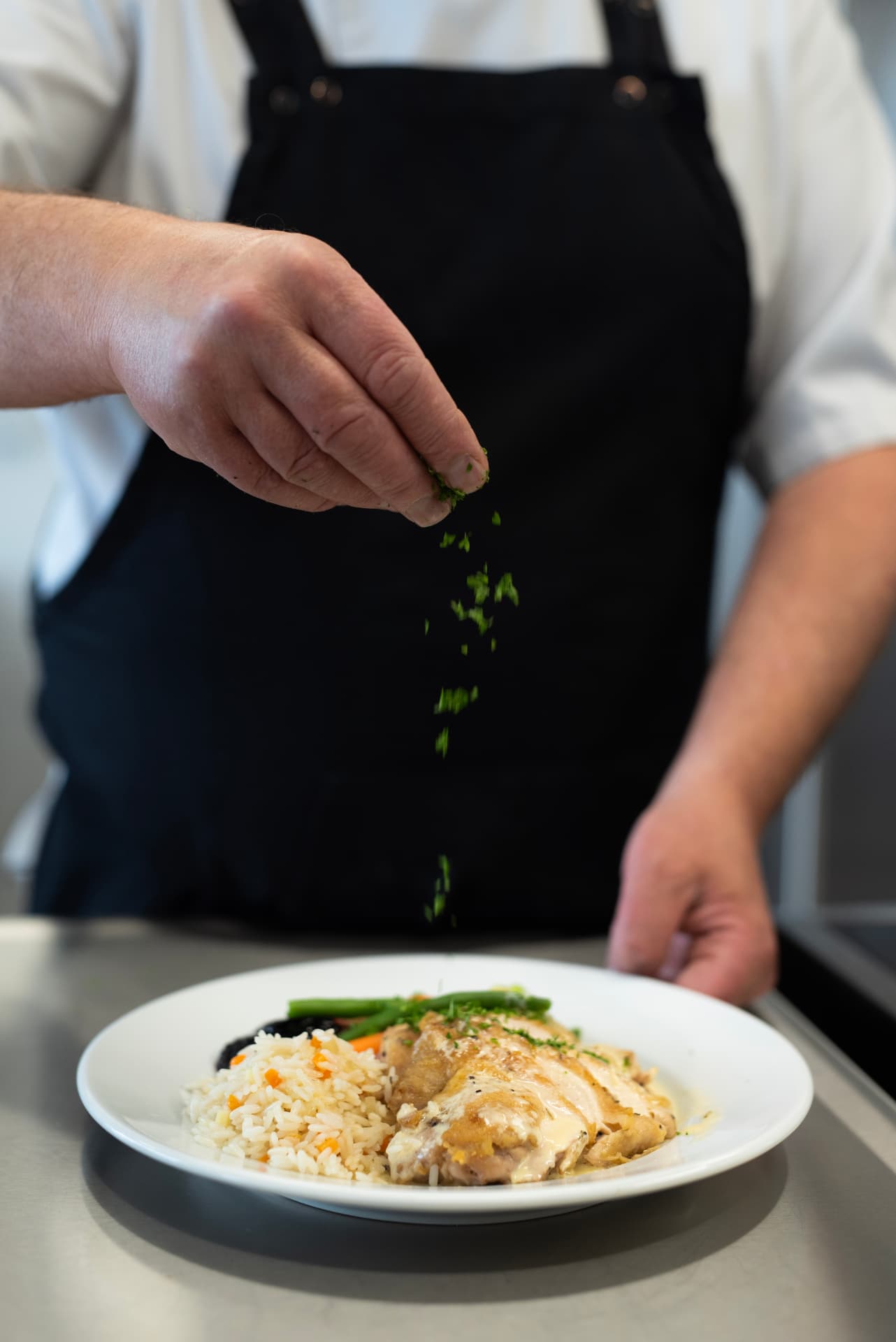 Kock strösslar färska örter över en vällagad lunchrätt